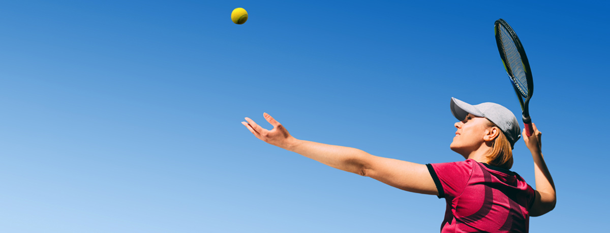 Middle aged woman throws a tennis ball up for a serve